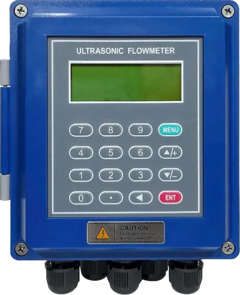 A Metrys clamp-on ultrasonic flow meter transmitter in a blue wall-mounted enclosure with a green LCD, a keypad and cable glands along its base.